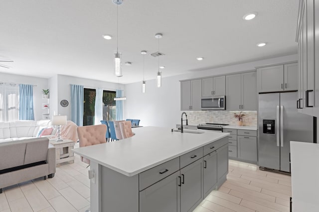 kitchen featuring sink, backsplash, decorative light fixtures, a center island with sink, and appliances with stainless steel finishes