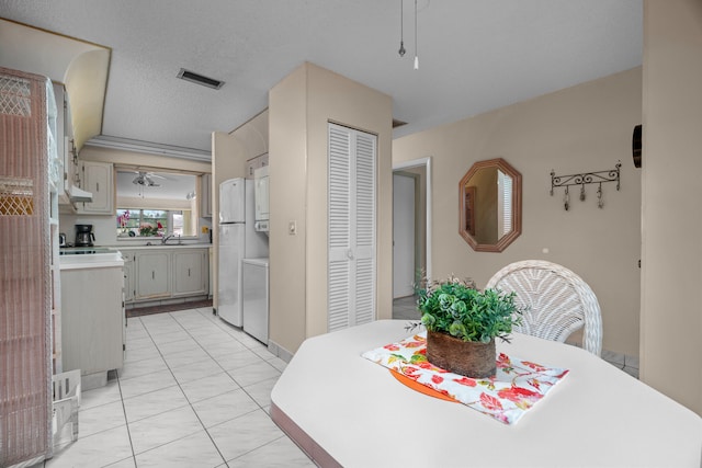 dining area featuring sink, light tile patterned floors, stacked washing maching and dryer, and a textured ceiling