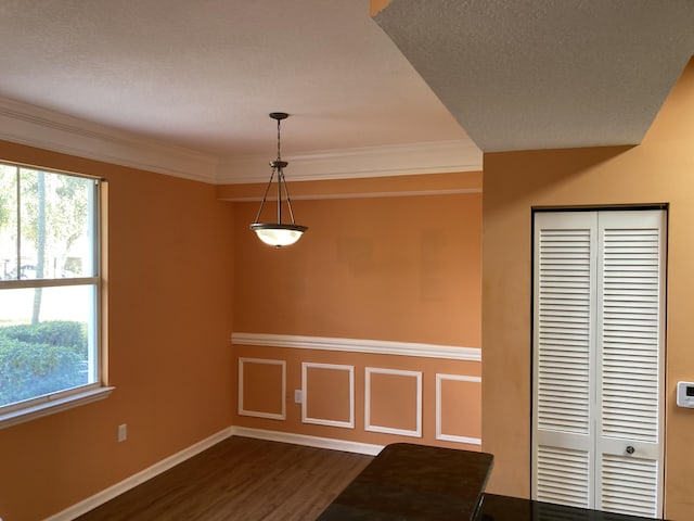 unfurnished dining area featuring a wealth of natural light, dark hardwood / wood-style flooring, a textured ceiling, and ornamental molding