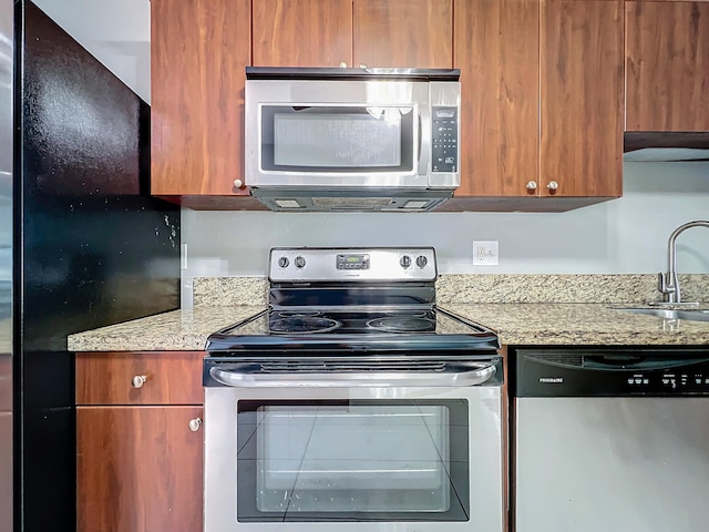 kitchen with stainless steel appliances, light stone counters, and sink