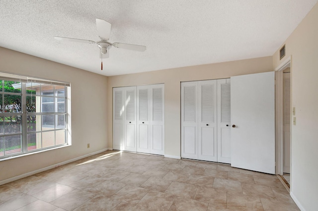 unfurnished bedroom featuring two closets, a textured ceiling, and ceiling fan