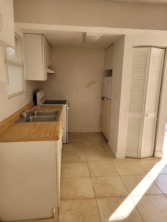 kitchen with sink, light tile patterned floors, white fridge, white cabinets, and range