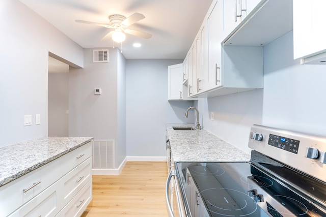 kitchen with light stone countertops, white cabinetry, sink, light hardwood / wood-style floors, and electric stove