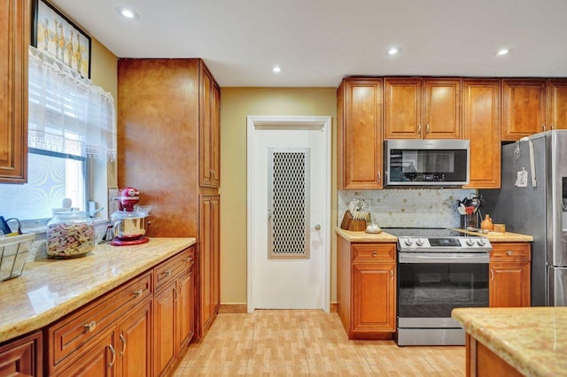 kitchen featuring decorative backsplash, light stone counters, light wood-type flooring, and appliances with stainless steel finishes