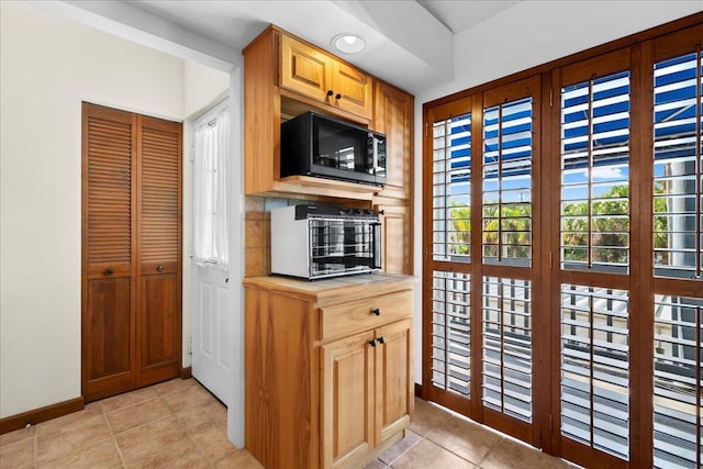 kitchen featuring black microwave, tile countertops, light tile patterned floors, a toaster, and baseboards