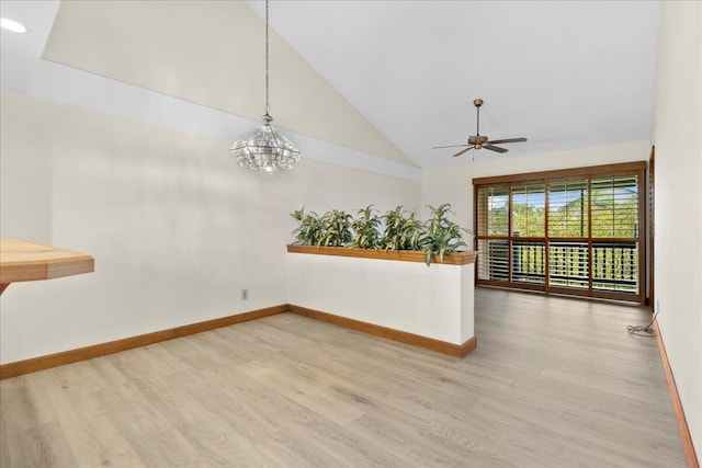 empty room with ceiling fan with notable chandelier, light wood-type flooring, and vaulted ceiling