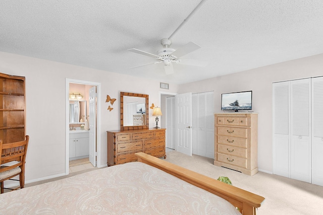 carpeted bedroom with a textured ceiling, ensuite bath, ceiling fan, and multiple closets