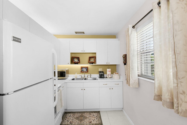 kitchen with light tile patterned floors, white refrigerator, white cabinetry, and sink