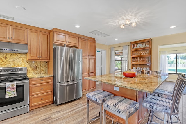 kitchen featuring light stone countertops, backsplash, appliances with stainless steel finishes, and a breakfast bar area