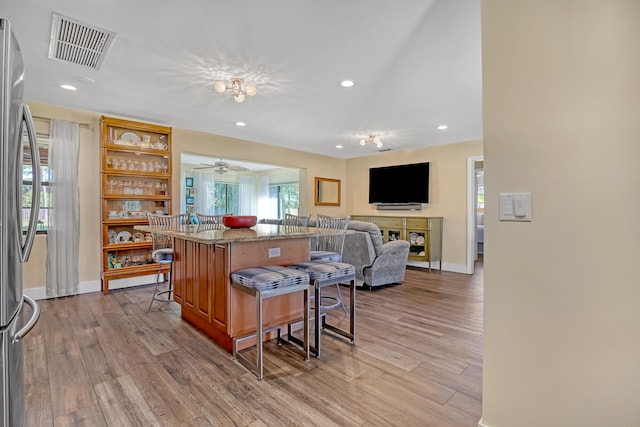 kitchen featuring light wood-type flooring, a breakfast bar area, ceiling fan, and stainless steel refrigerator