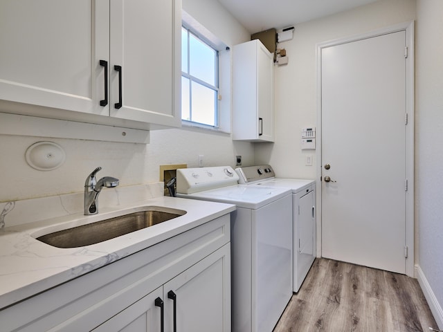 clothes washing area with washing machine and dryer, sink, cabinets, and light hardwood / wood-style floors