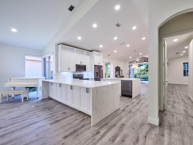 kitchen with appliances with stainless steel finishes, vaulted ceiling, decorative light fixtures, white cabinetry, and a large island