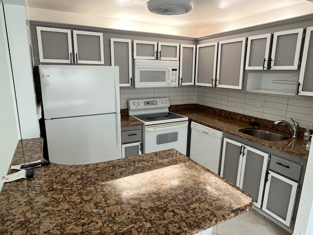 kitchen with sink, backsplash, dark stone counters, white appliances, and gray cabinets