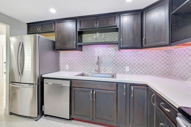 kitchen with appliances with stainless steel finishes, backsplash, dark brown cabinets, sink, and light tile patterned floors