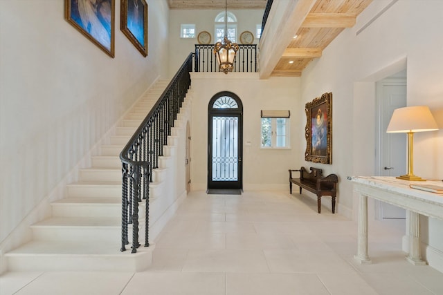 tiled entrance foyer with beam ceiling, a towering ceiling, wood ceiling, and an inviting chandelier