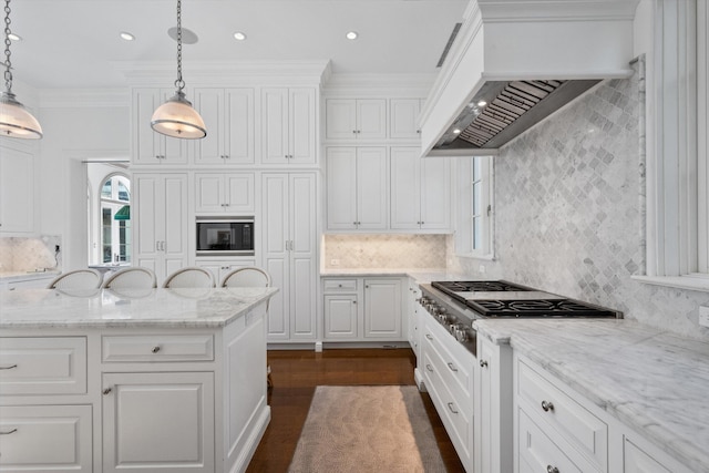 kitchen with custom range hood, black microwave, decorative light fixtures, white cabinets, and stainless steel gas stovetop