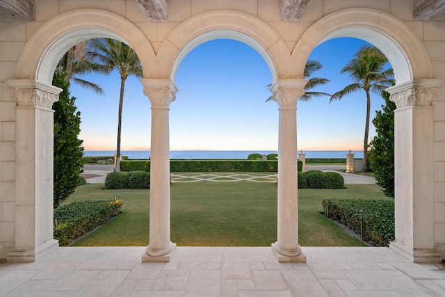 patio terrace at dusk featuring a lawn and a water view