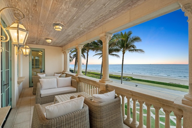 balcony at dusk featuring a water view and a view of the beach