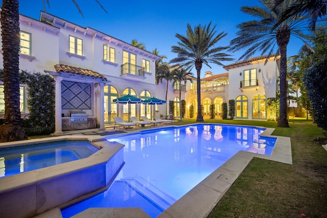 pool at dusk with an in ground hot tub, area for grilling, and a lawn