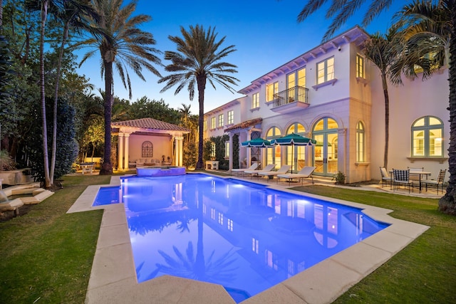 pool at dusk featuring an in ground hot tub and a patio