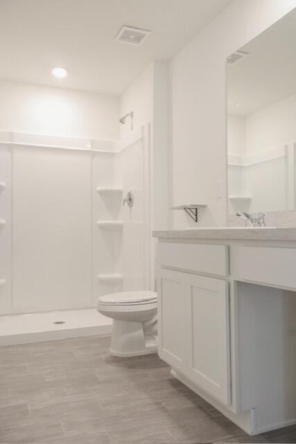 bathroom with a shower, vanity, hardwood / wood-style flooring, and toilet