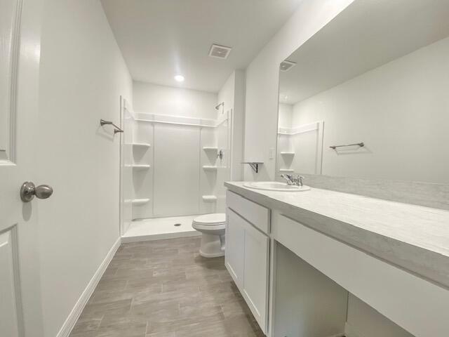 bathroom featuring toilet, a shower, and vanity