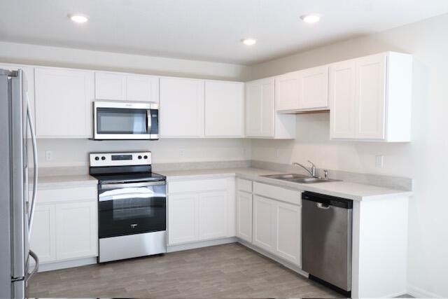 kitchen with white cabinets, stainless steel appliances, light hardwood / wood-style flooring, and sink