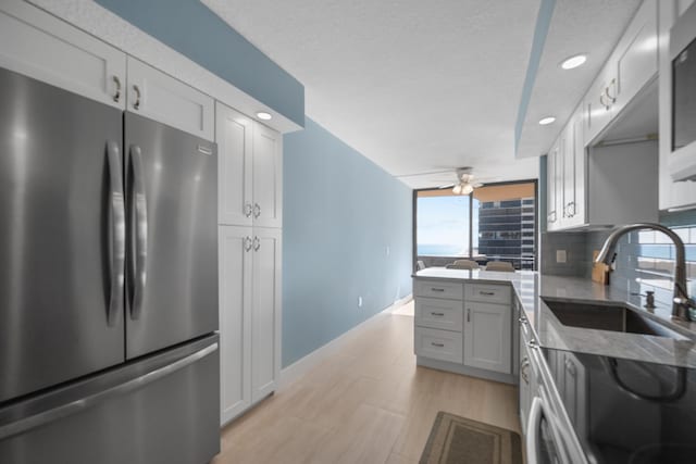 kitchen with backsplash, white cabinets, sink, ceiling fan, and stainless steel fridge