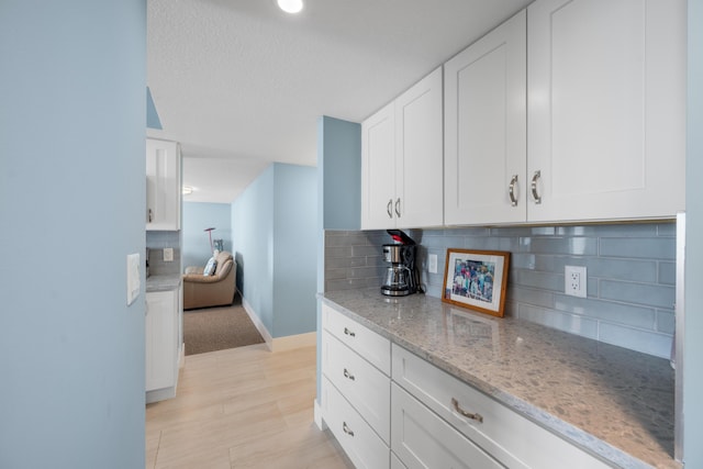 kitchen with a textured ceiling, tasteful backsplash, white cabinetry, and light stone counters