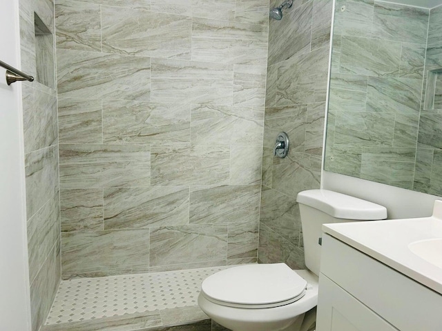 bathroom with toilet, a tile shower, and vanity