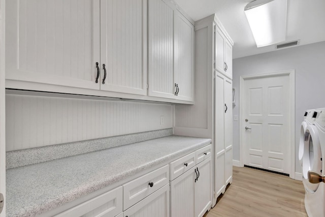 laundry area featuring washer and clothes dryer, light hardwood / wood-style floors, and cabinets