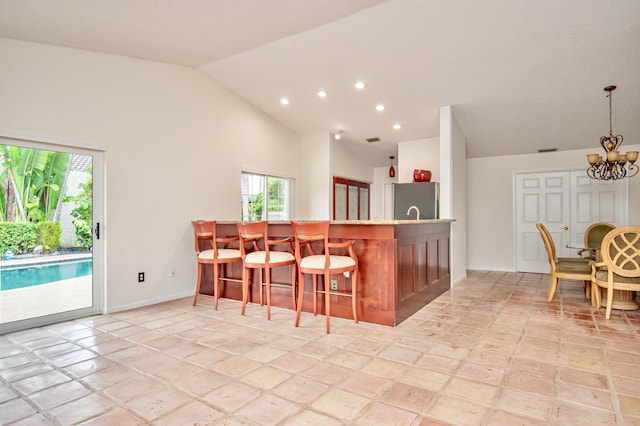 kitchen with stainless steel refrigerator, a kitchen breakfast bar, high vaulted ceiling, a chandelier, and decorative light fixtures