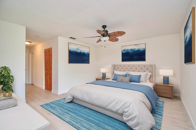 bedroom with ceiling fan, a closet, light hardwood / wood-style floors, and a textured ceiling