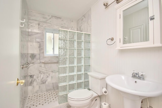 bathroom with a tile shower, toilet, and sink