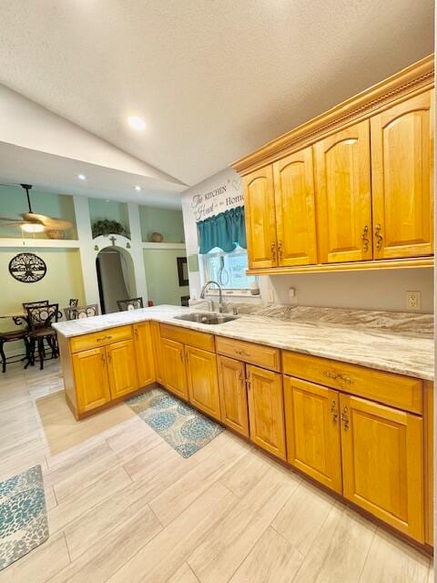 kitchen with kitchen peninsula, a textured ceiling, vaulted ceiling, sink, and light hardwood / wood-style flooring