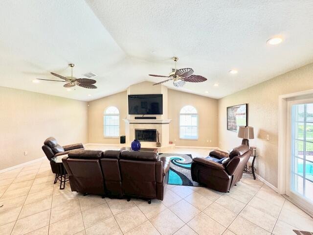 tiled living room with a textured ceiling, ceiling fan, a healthy amount of sunlight, and vaulted ceiling