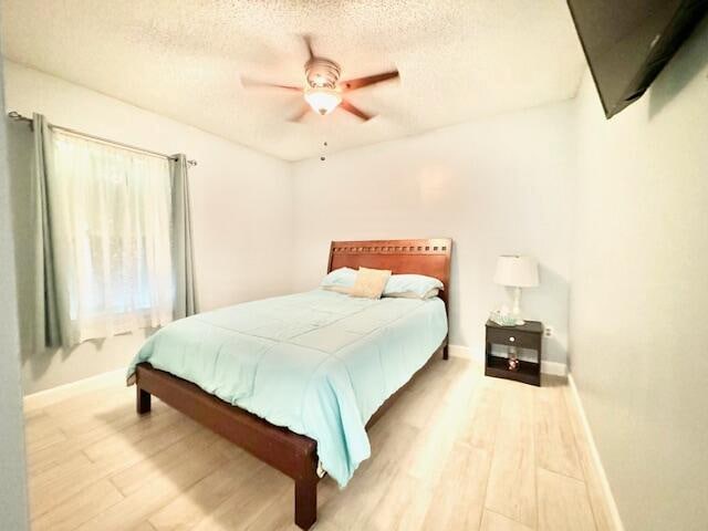 bedroom with a textured ceiling, light hardwood / wood-style floors, and ceiling fan