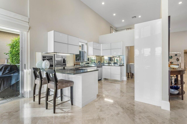 kitchen featuring a breakfast bar, stainless steel appliances, sink, a high ceiling, and white cabinetry