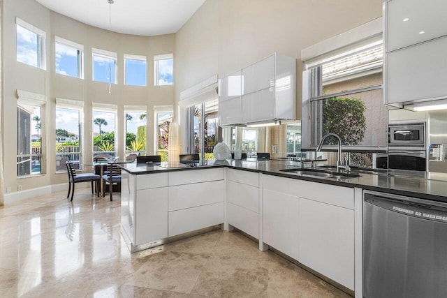 kitchen featuring kitchen peninsula, appliances with stainless steel finishes, a towering ceiling, sink, and white cabinetry