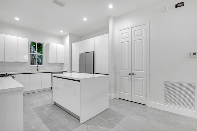 kitchen featuring white cabinets, stainless steel fridge, a kitchen island, and sink