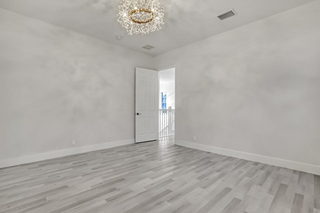 spare room with a chandelier and light wood-type flooring