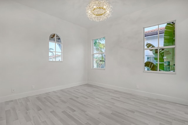 empty room with a wealth of natural light, light hardwood / wood-style floors, and an inviting chandelier