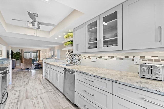 kitchen with a sink, glass insert cabinets, appliances with stainless steel finishes, decorative backsplash, and a raised ceiling