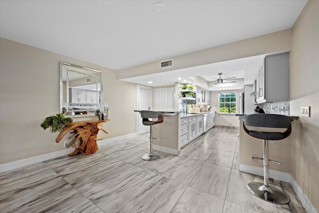 kitchen with visible vents, a tray ceiling, ceiling fan, a sink, and a kitchen breakfast bar