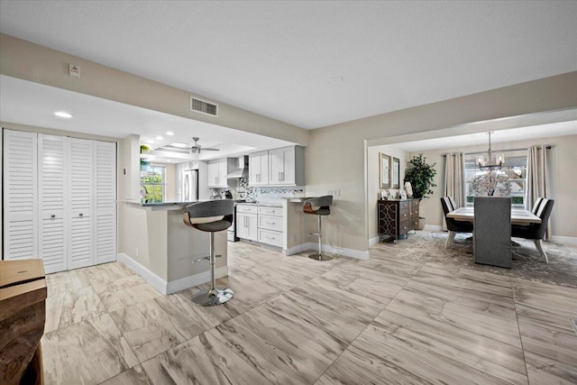 kitchen with visible vents, a breakfast bar, a peninsula, white cabinets, and wall chimney exhaust hood