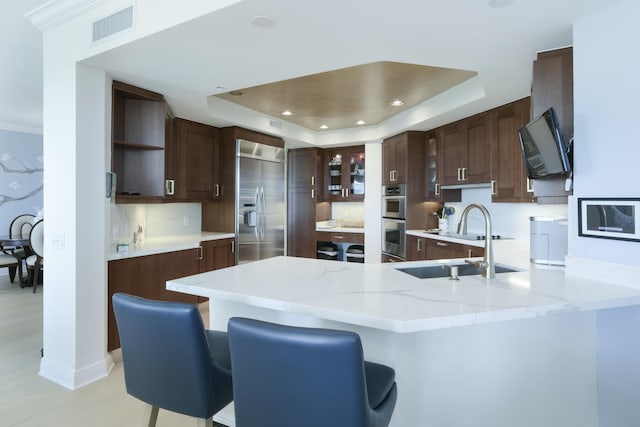 kitchen featuring a raised ceiling, sink, appliances with stainless steel finishes, a kitchen bar, and kitchen peninsula