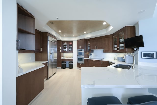 kitchen with a breakfast bar, a raised ceiling, kitchen peninsula, and stainless steel appliances