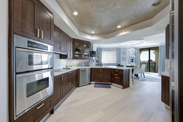 kitchen with pendant lighting, an inviting chandelier, light hardwood / wood-style flooring, appliances with stainless steel finishes, and a tray ceiling