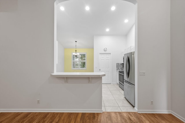 kitchen with pendant lighting, a kitchen bar, appliances with stainless steel finishes, and light hardwood / wood-style flooring