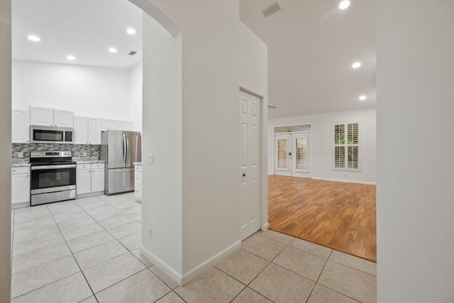 kitchen with decorative backsplash, white cabinets, light tile patterned floors, and appliances with stainless steel finishes